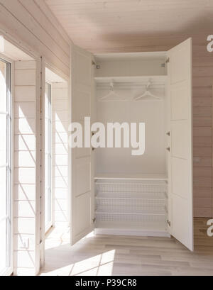 Apartamentos de estilo escandinavo. Luz interior del dormitorio en una casa de madera orgánicos de color blanco. Muebles de Ikea, armario. Piso de madera, paredes, techos de madera. Armario blanco. Ventanas panorámicas Foto de stock