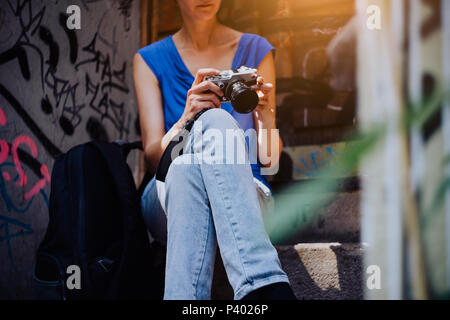 Mujer joven sentada en las escaleras, sosteniendo la cámara vintage y mirando a las fotos hechas en el tour por la ciudad