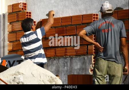 Em construção Pedreiros levantando parede de tijolos.