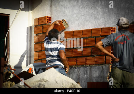 Em construção Pedreiros levantando parede de tijolos.