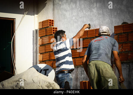Em construção Pedreiros levantando parede de tijolos.