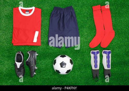 Una disposición laicos plana de fútbol o soccer kit en el césped, con camisa, pantalones, calcetines, botas, espinilleras y bola.