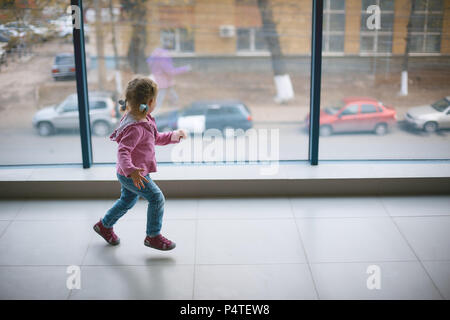 Una niña corre alrededor del nuevo apartamento grande cerca de una ventana panorámica Foto de stock