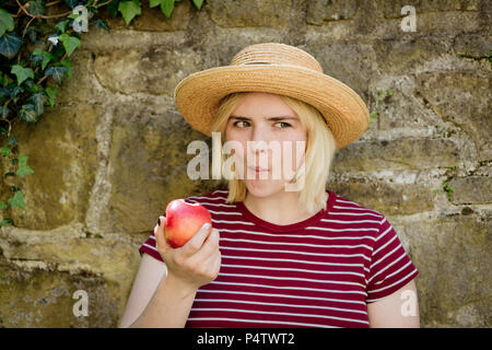 Retrato de joven mujer rubia con sombrero para el sol comiendo apple