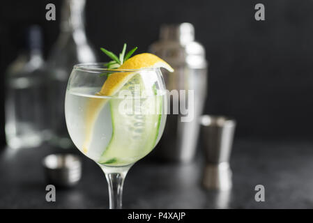 Gin Fizz cóctel con limón, pepino, Romero y el hielo. Gin Tonic o gimlet sobre fondo negro, copie el espacio. Foto de stock