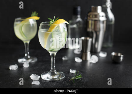 Gin Fizz cóctel con limón, pepino, Romero y el hielo. Gin Tonic o gimlet sobre fondo negro, copie el espacio. Foto de stock