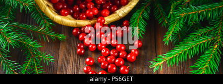 Cowberry, foxberry, arándano, Arándano rojo sorbos de la cesta sobre una tabla de madera marrón. Rodeado de ramas de abeto.