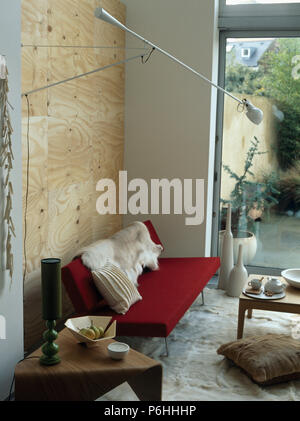 Tabla de madera y triangular pequeño sofá rojo con faux wolfskin throw en salón moderno con paredes de madera contrachapada Foto de stock