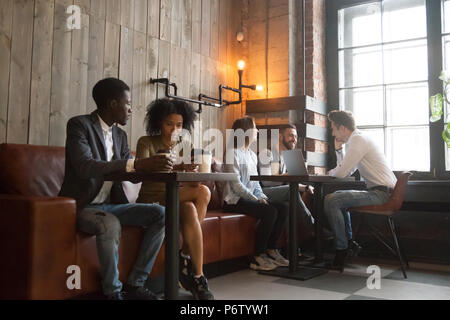 Los millennials multirracial disfrutando de café trabajando en gadgets en co