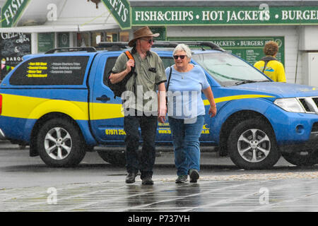 West Bay, Dorset, Reino Unido. 4 de julio de 2018. El clima del Reino Unido. Una pareja en la ciudad balnearia de West Bay en Dorset no demasiado molesta por la lluvia durante una ducha. Crédito de la imagen: Graham Hunt/Alamy Live News Foto de stock