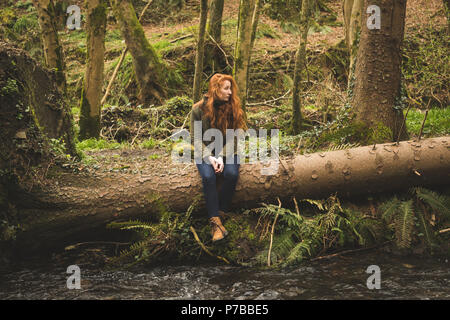 Excursionista femenina sentada en el tronco del árbol caído cerca del río