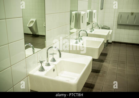 Baño público masculino elegante blanco con lavabos y orinal reflejando en el espejo Foto de stock