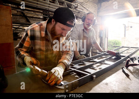 Senior herrero e hijo de martilleo metálico en workbench en herreros shop