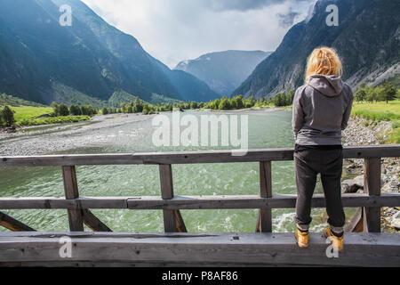 Vista posterior del joven parado en el puente de madera y mirando al hermoso río de montaña, Altai, Rusia