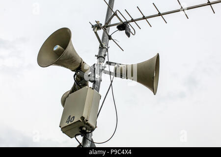 Sistema de megafonía altavoces en un polo, la antena y la caja con el número 46 parcialmente despegado, cielo nublado en segundo plano.