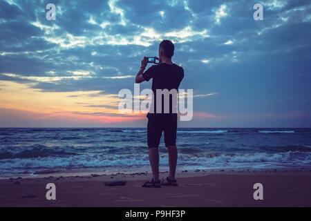 Silueta de hombre conservar recuerdos con la cámara del teléfono en su mano. Maravillosa puesta de sol en el mar, buen nivel de agua