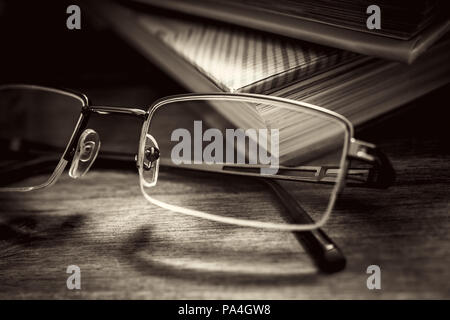 Las gafas delante de algunos libros sobre la mesa de madera en colores monocromáticos Vintage Foto de stock