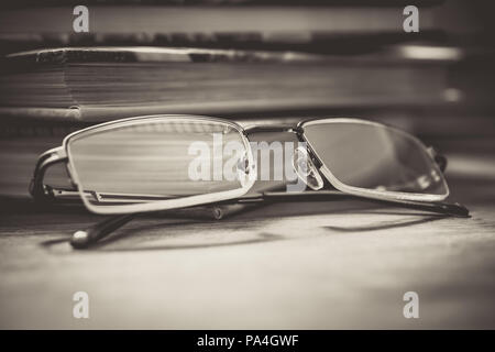 Par de gafas delante de algunos libros sobre la mesa de madera en la noche en colores monocromáticos Foto de stock