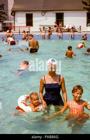 Mujer con un traje de baño de una pieza y un gorro de baño florido con niños pequeños en una piscina ocupada en verano, Briarcliff Manor piscina local, condado de Westchester, Nueva York, EE.UU. En la década de 1960