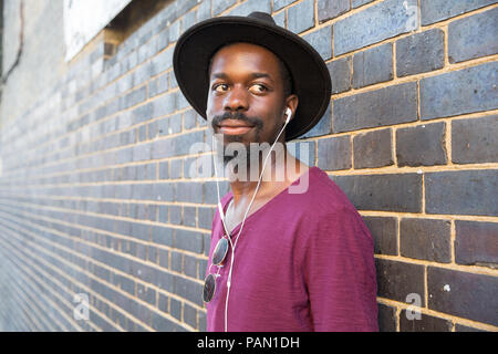 Un hombre negro cool Hipster, vistiendo un sombrero de ala grande, morado  camiseta y auriculares, apoyado contra una pared en Brick Lane, Shoreditch,  Londres Fotografía de stock - Alamy
