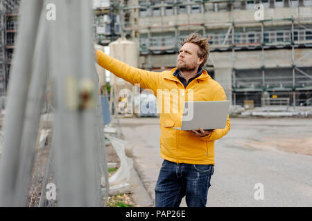 Hombre sujetando portátil, sitio de construcción en el fondo Foto de stock
