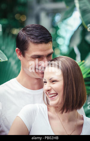 Retrato de dos personas, hombre mujer chica juntos, de pie entre los árboles verdes plantas en parque afuera, sonriendo riendo abrazar, mirar lejos, íntimo m Foto de stock