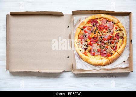 Pizza fresca en una caja de cartón en la mesa de madera blanca, vista superior. Desde arriba, plano laical. Foto de stock