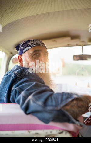 Altos hipster tatuados con una barba blanca sentado en su camioneta Foto de stock