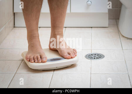 Imagen recortada del hombre pies de pie sobre una báscula, en el piso del baño Foto de stock