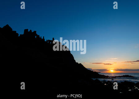 Ruinas del Castillo de Dunluce recortadas por el sunsetting en la costa irlandesa Foto de stock
