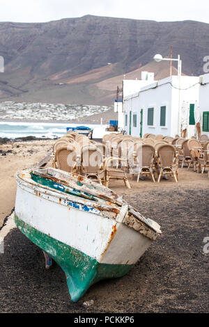 La caleta de Famara, Lanzarote, Palmas/España: barco de pesca de orilla y vacío, restaurante al aire libre, con el mar de fondo