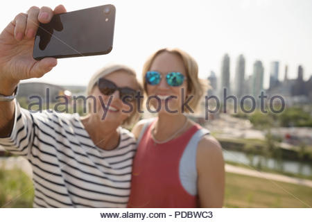 Madre e hija sonriente tomando en sunny selfie parque urbano