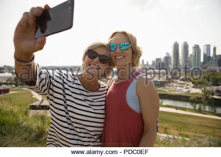 Madre e hija sonriente tomando en sunny selfie parque urbano
