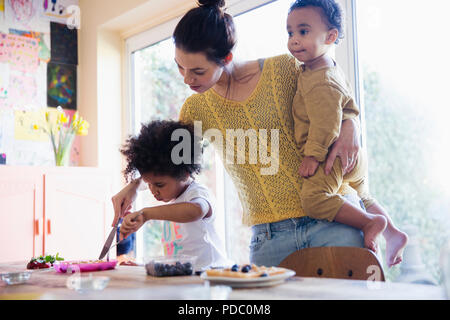 Madre ayudando a infante hija desayuno waffles de corte Foto de stock