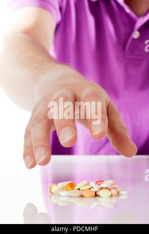 Mano de hombres caucásicos en camisa púrpura llegando a un montón de píldoras y cápsulas Foto de stock