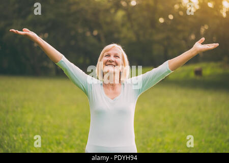 Senior mujer disfruta con sus brazos extendidos en la naturaleza.Imagen es intencionalmente tonificado.