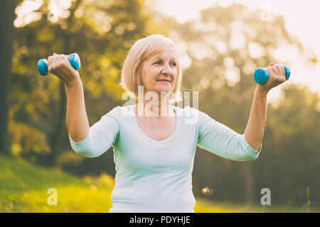 Mujer senior deportivo el ejercicio con pesas outdoor.Imagen es intencionalmente tonificado.