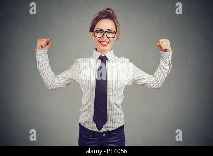 Bastante decidida mujer en camisa y corbata mostrando bíceps y mirando alegremente a la cámara siendo fuertes y motivados