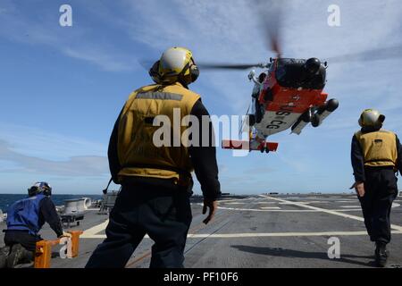 Un Servicio de Guardacostas MH-60 Jayhawk tripulaciones de helicóptero realiza una serie de desembarques de cubierta en la cubierta de vuelo del misil guiado por el destructor USS Momsen (DDG-92) cerca de Kodiak, Alaska, el 14 de agosto, 2018. El chaleco amarillo designa el desembarco signalman; esta persona se dedica a ayudar a la tripulación Jayhawk con aterrizaje correctamente y de forma segura a bordo del barco en movimiento en el mar. La Guardia Costera de EE.UU. Foto de Suboficiales de 3ª clase Lauren Dean. Foto de stock
