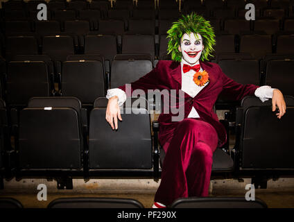 Un cosplayer masculino vestidos como el Joker del Batman y DC Comics franquicia sentado solo en una sala de cine abandonada y mirando amenazante