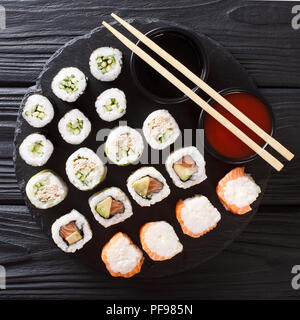 Menú japonés de rollos con salmón, atún, aguacate, pepino servidos con salsas de cerca en una losa de piedra. top vista desde arriba Foto de stock