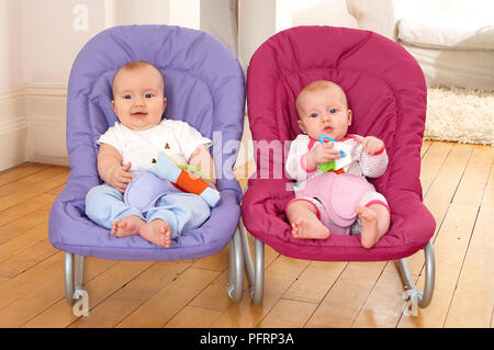 Twin Baby Boy y Girl sentados en sillas saltarinas jugar con juguetes, vista frontal, 1 año