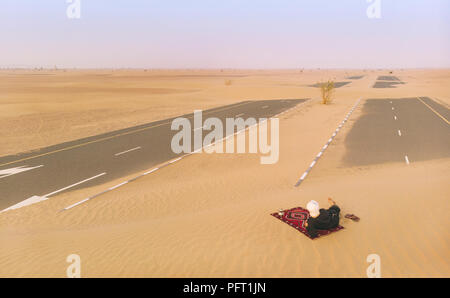 Hombre tuareg beber té en un desierto, buscando un camino cubierto de arena Foto de stock