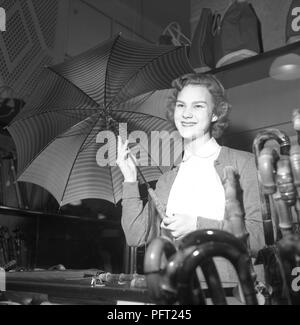 Paraguas en la década de 1950. Una joven trabaja en una tienda como salesclerk. Ella demuestra una de las sombrillas para un cliente. S. Steéns Speceri & Diversehandel Suecia 1952 ref 2252 Foto de stock