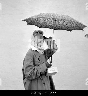 1950 MUJER con sombrilla. Una joven mujer sosteniendo un paraguas en un día lluvioso. Suecia 1955 Foto de stock