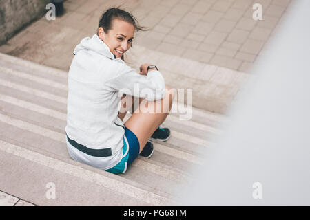 Deportivo sonriente joven sentado en las escaleras exteriores