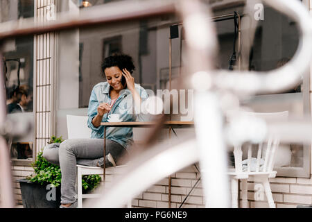 Mujer joven bebiendo café en frente de la cafetería, hablando por el teléfono