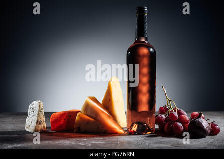 Botella de vino tinto, diferentes tipos de quesos y uvas en gris