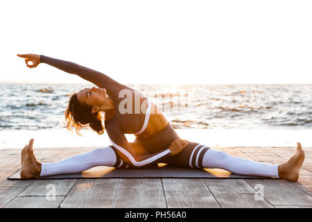 Imagen de la joven dama de fitness al aire libre en la playa, hacer yoga ejercicios de estiramiento.