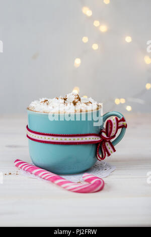 Sabroso café con crema en una taza de cerámica azul con cinta y caña de Navidad sobre fondo blanco con bokeh Foto de stock